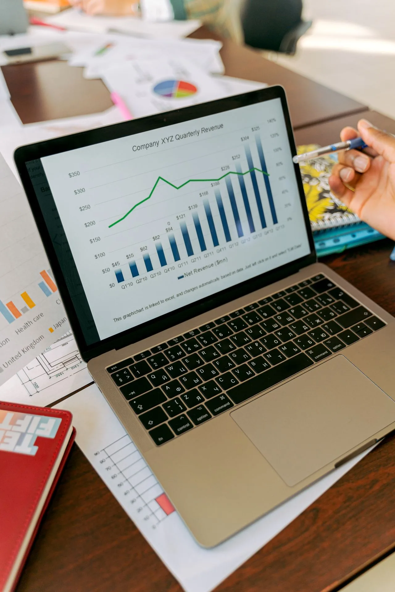 A laptop showing a quarterly revenue chart beside printed reports