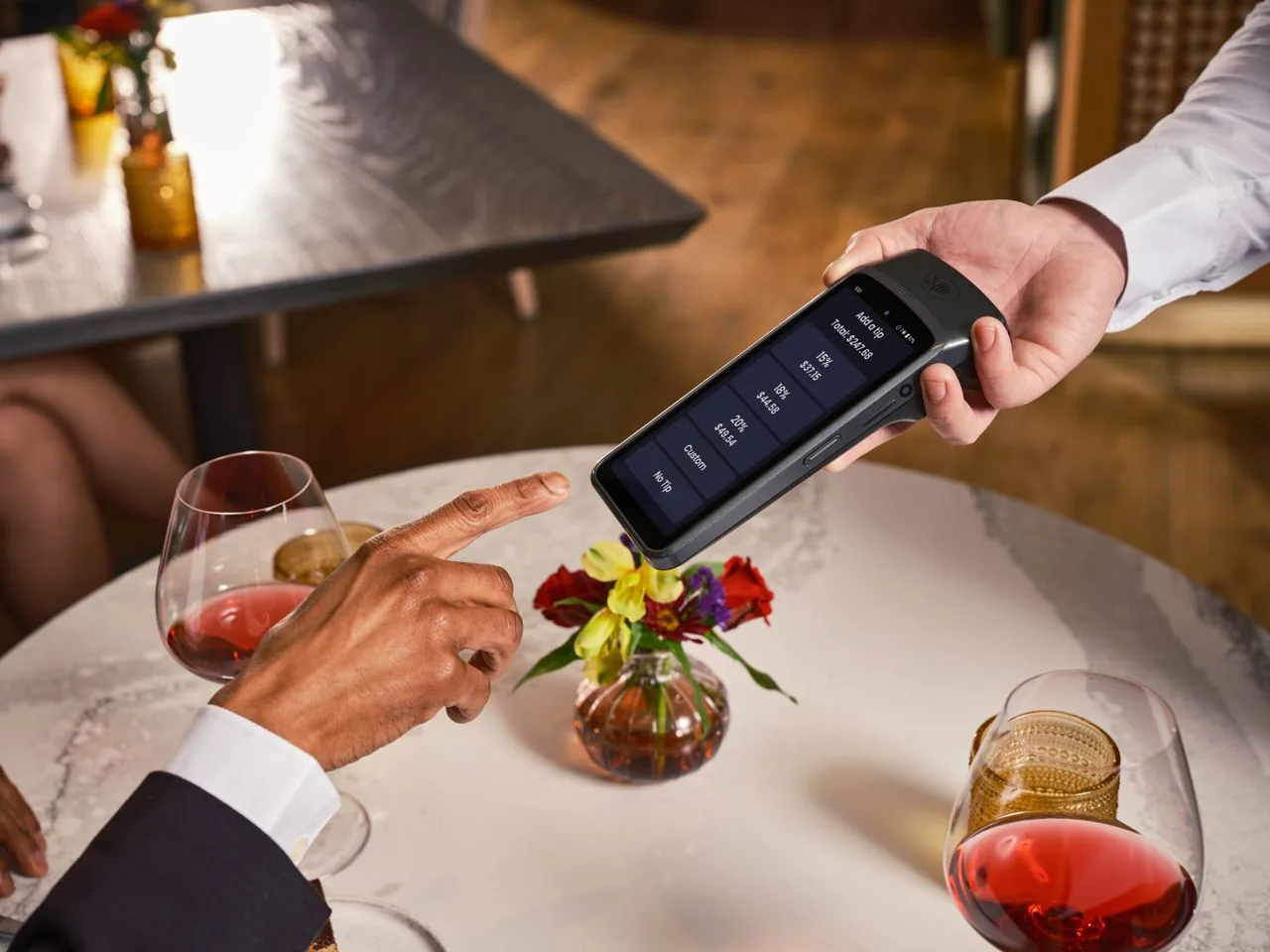 A guest paying by card on a handheld terminal at a laid table