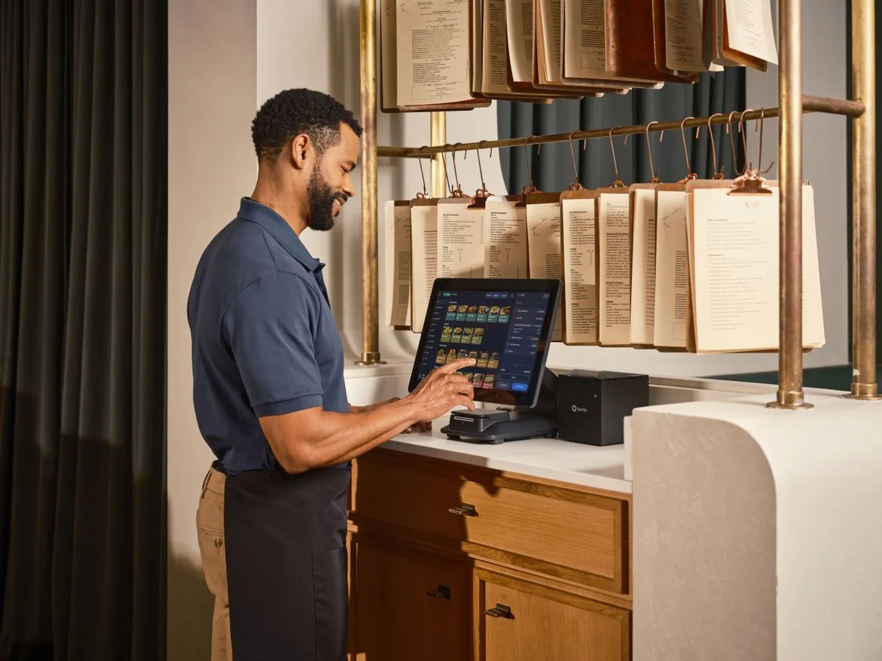 A server working at a POS terminal beside a rail of kitchen tickets